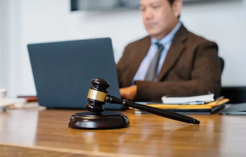 Sądowy młotek na biurku, prawnik pracuje przy laptopie. Dyskrecja w ujawnieniu informacji o zadłużeniu osobom trzecim.